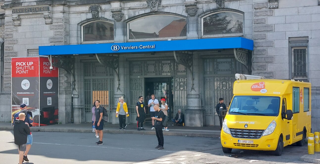 The station's main entrance. To the left is the pickup point for the shuttle busses, on the right is a yellow van that sells bus tickets.